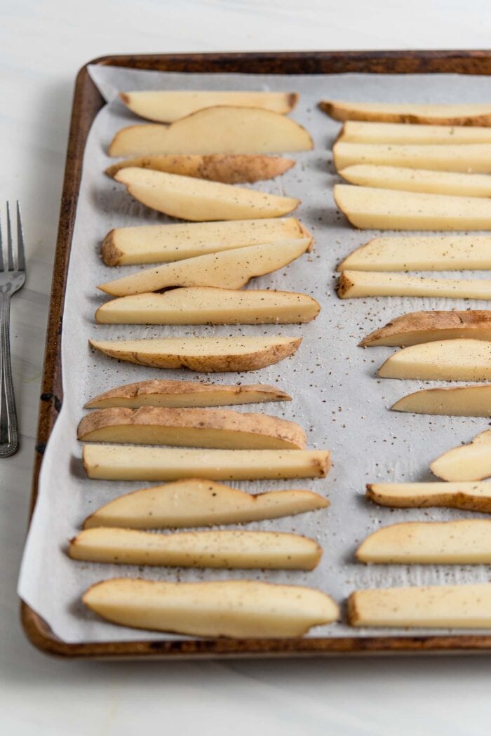 Sliced potato wedges spread out on a baking tray.