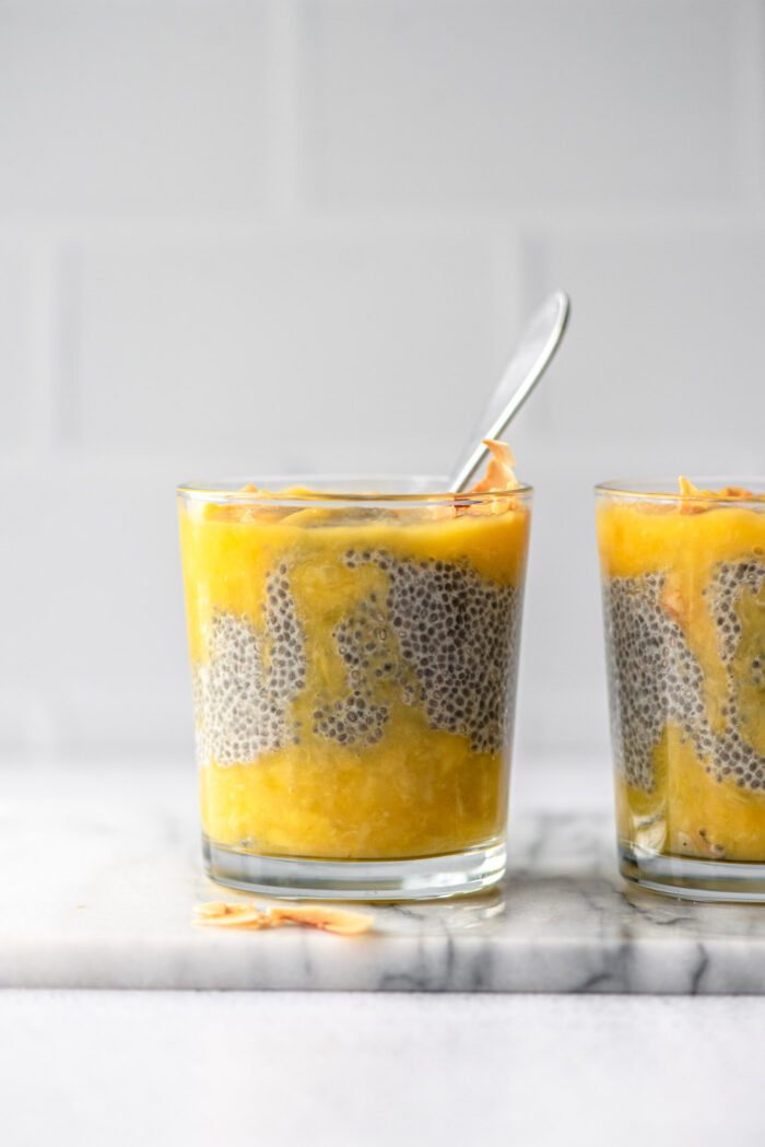 Two jars of chia seed pudding layered with mango puree and topped with coconut flakes.