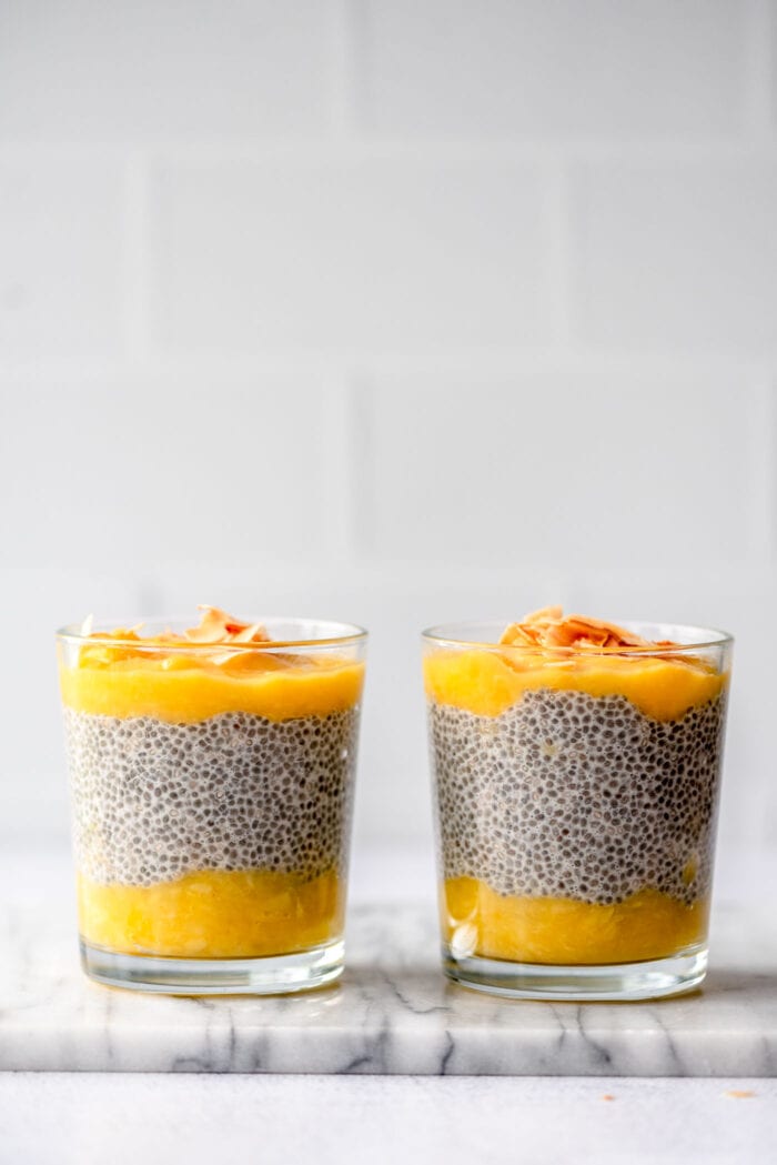 Two jars of chia pudding between layers of mango puree.