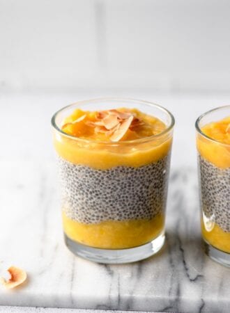 A glass jar of layered mango chia pudding topped with coconut flakes. Another jar of pudding is in the background.