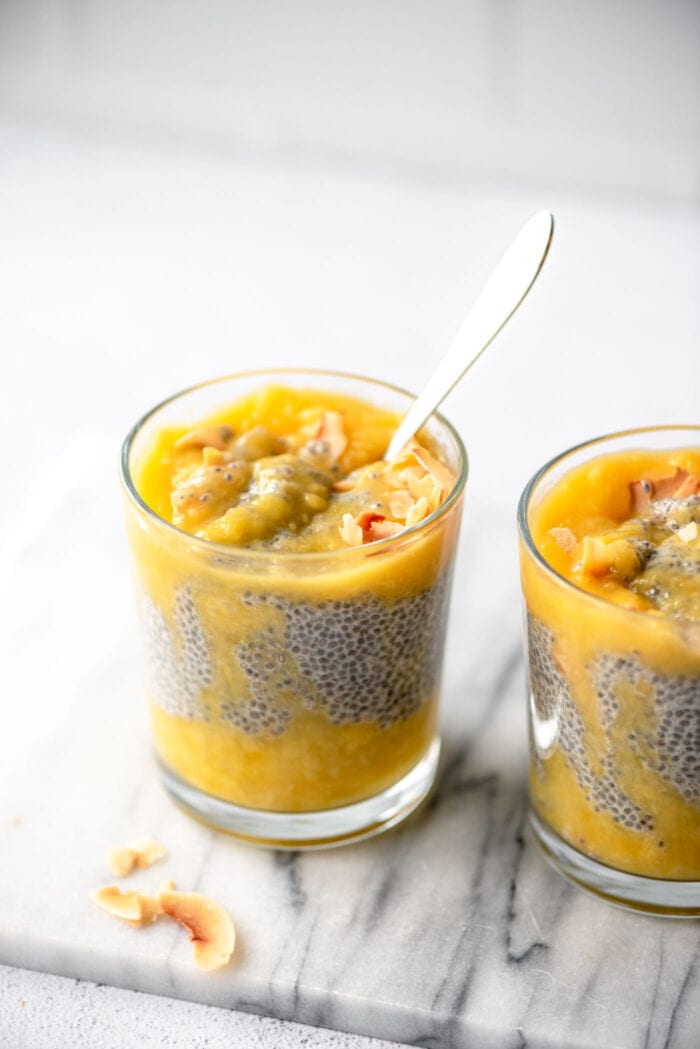 Two jars of chia seed pudding layered with mango puree and topped with coconut flakes.