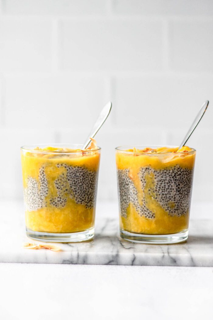 Two glass jars of layered mango chia pudding with spoons in them.