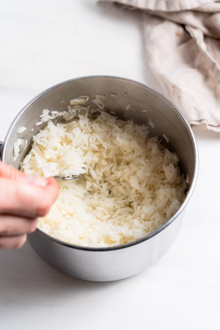 Cooked white rice being fluffed with a fork in a small saucepan.