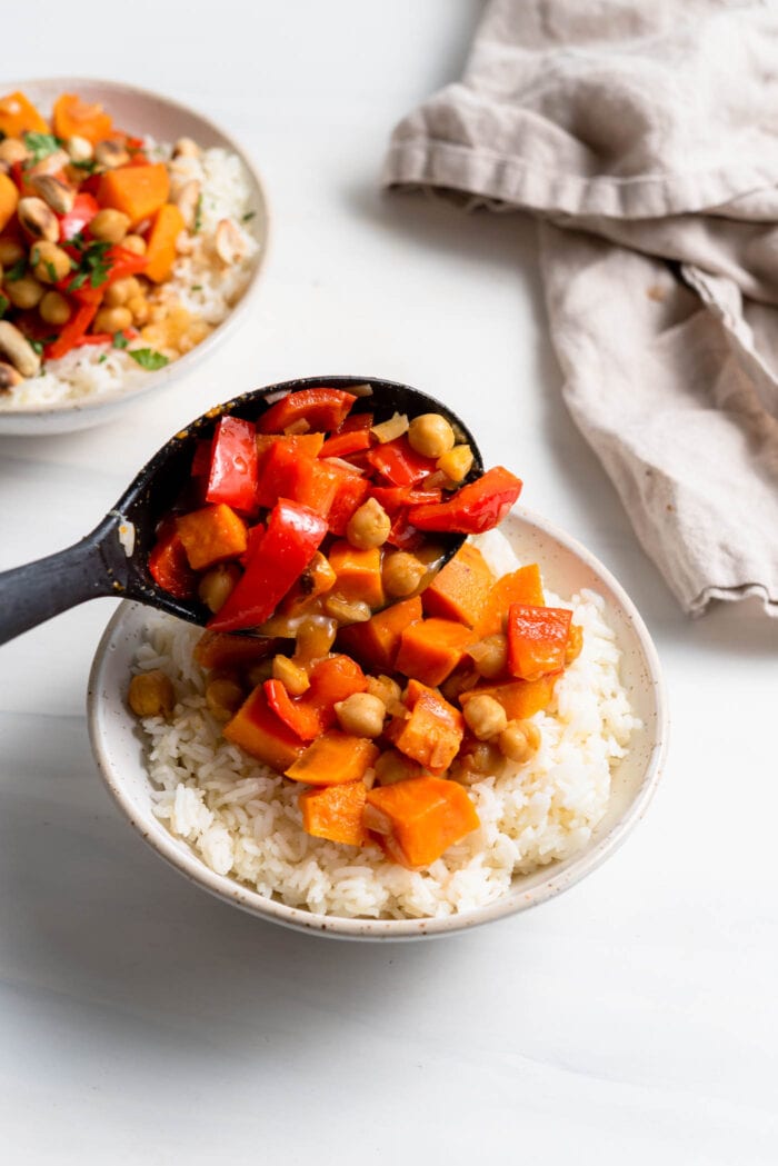 Adding a scoop of sweet potato curry to a bowl of rice.