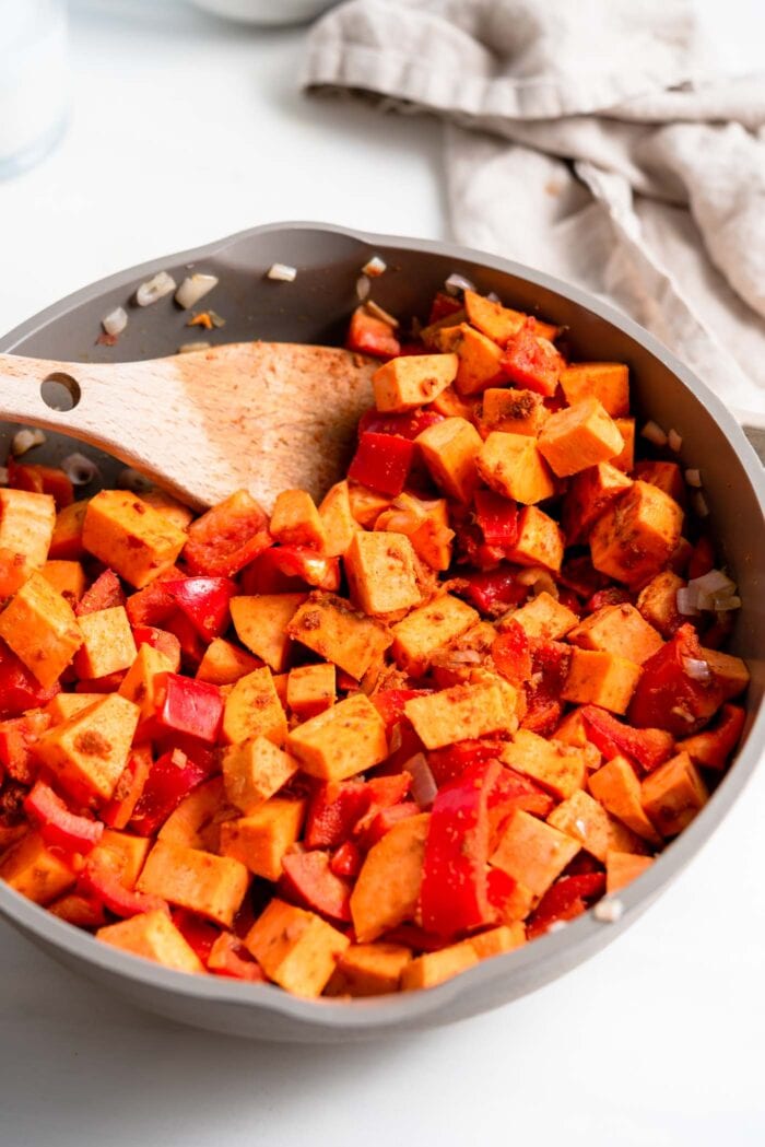 Sweet potato and bell pepper cooking in spices in a skillet.