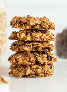 Stack of 5 oatmeal chocolate chips cookies with jars of oats and chocolate chips in the background.