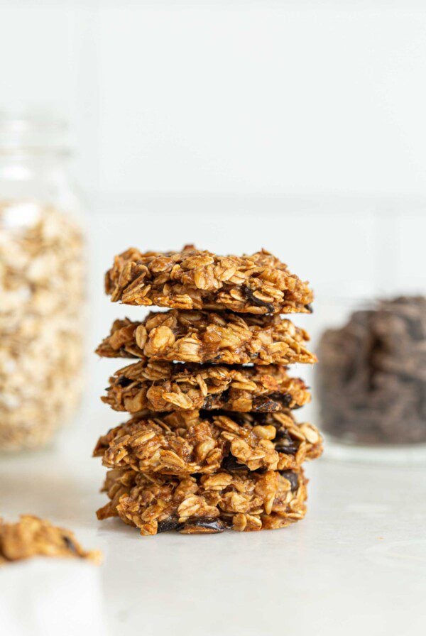 Stack of 5 oatmeal chocolate chips cookies with jars of oats and chocolate chips in the background.