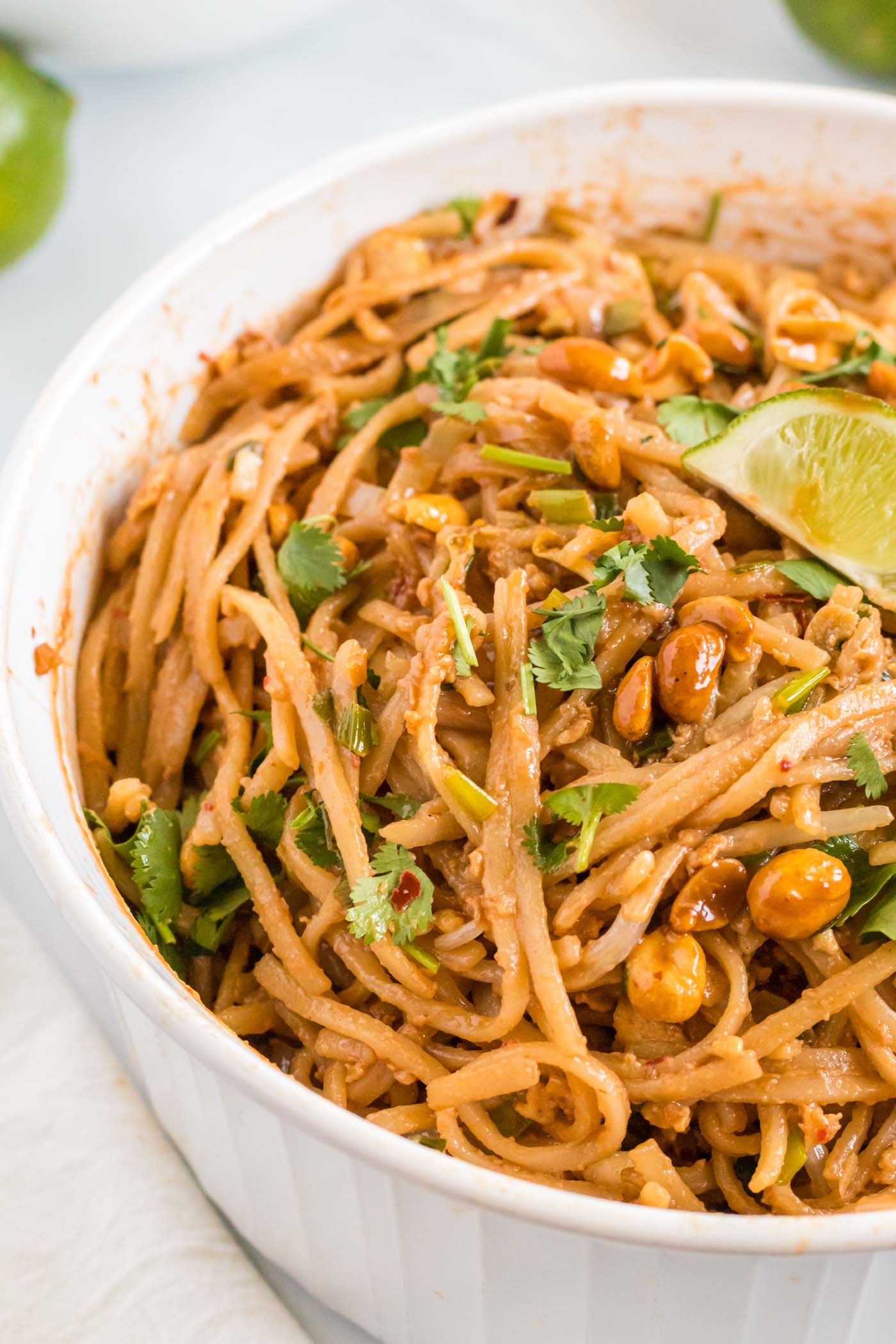 Close up of vegan tofu pad thai in a bowl topped with lime, peanuts and cilantro.