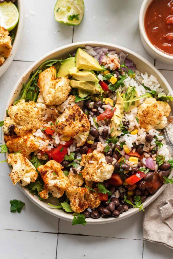 Overhead view of a burrito bowl with rice, roasted cauliflower, avocado and black beans.