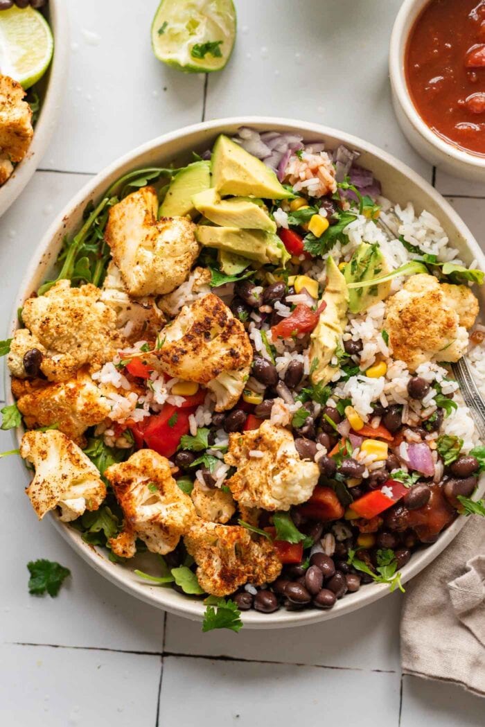 Overhead view of a burrito bowl with rice, roasted cauliflower, avocado and black beans.