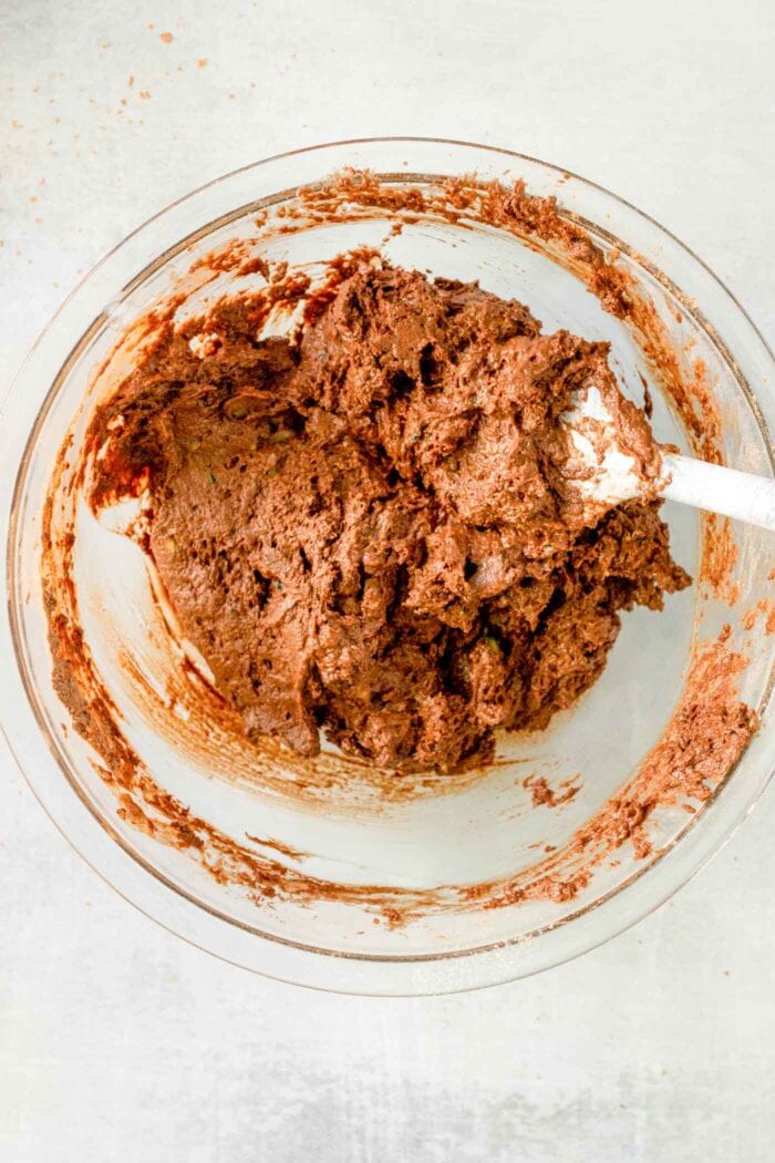 A thick chocolate batter being mixed with a wooden spoon in a mixing bowl.