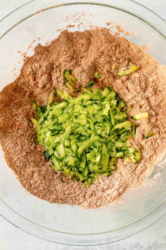 Grated zucchini with flour and cocoa powder in a glass mixing bowl.