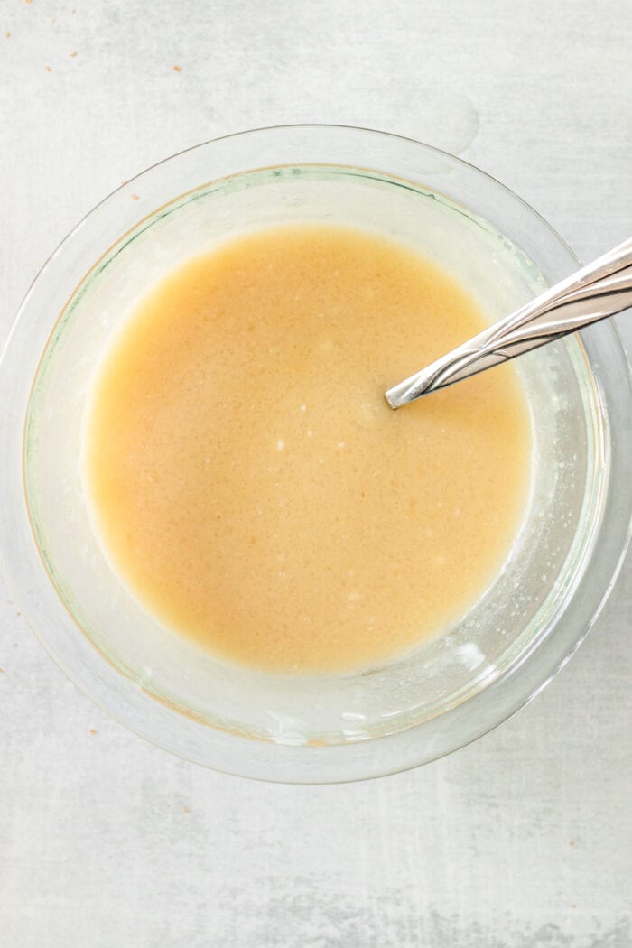 Maple syrup, applesauce and coconut yogurt mixed together in a glass mixing bowl with a spoon.