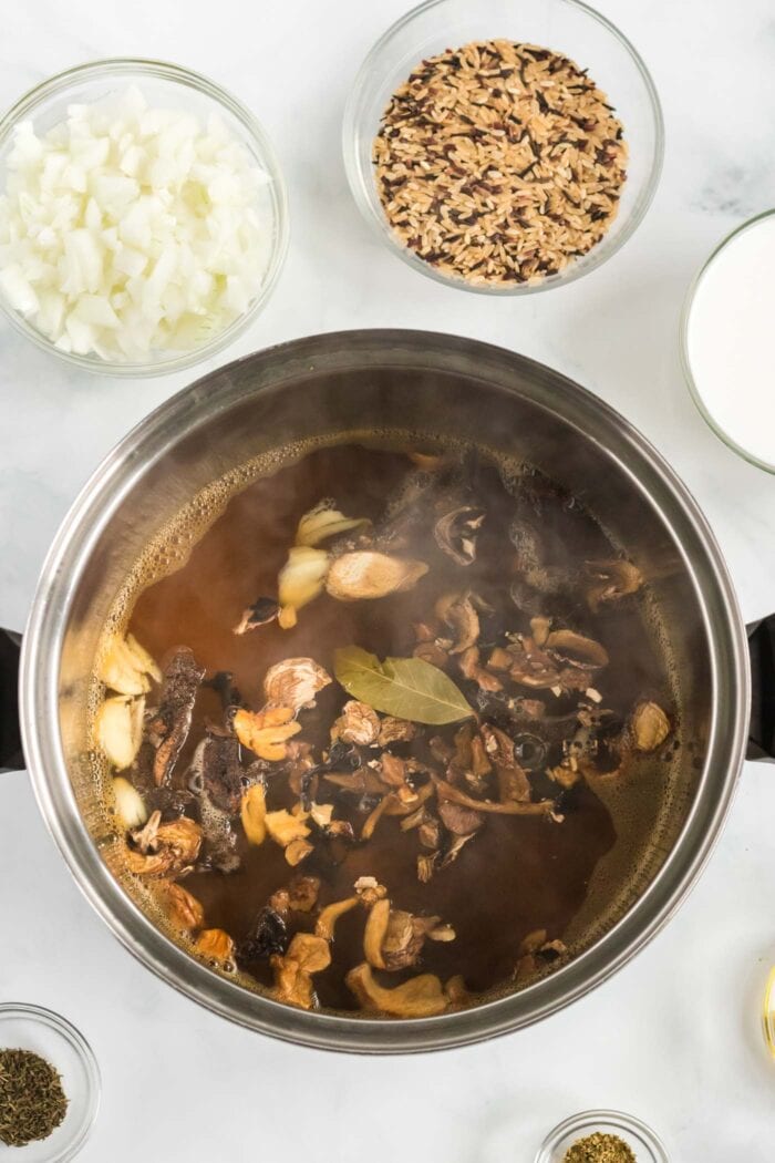Vegetable broth in a pot with chopped wild mushrooms and a bay leaf.