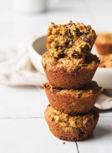Stack of four chocolate chip zucchini muffins. Muffin on top is cut in half to show inside texture.