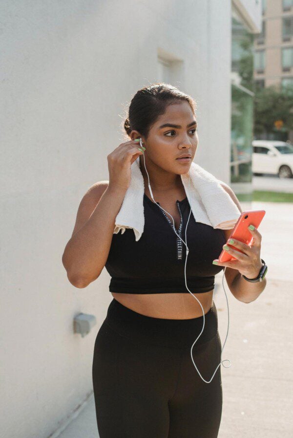 Woman in workout gear with headphones in plugged into an iPhone.