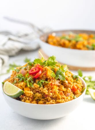Large bowl of curried quinoa with chickpeas and sweet potato topped with sliced chilis and cilantro.