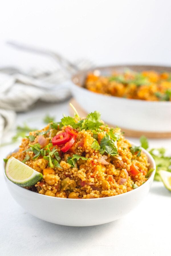 Large bowl of curried quinoa with chickpeas and sweet potato topped with sliced chilis and cilantro.