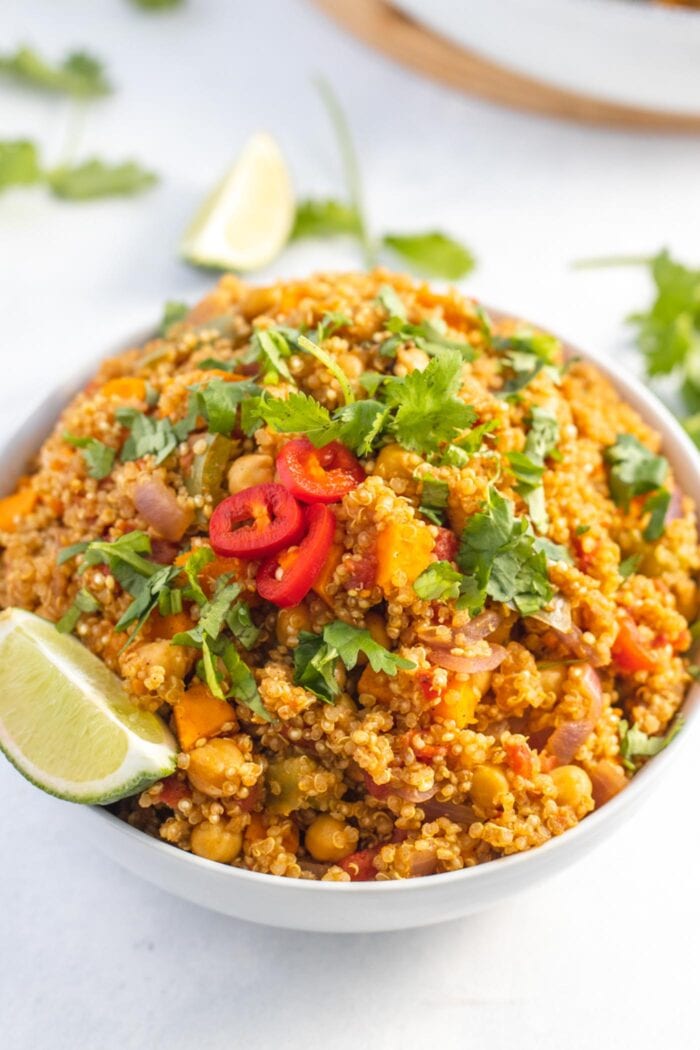 Large bowl of curried quinoa with chickpeas and sweet potato topped with sliced chilis and cilantro.