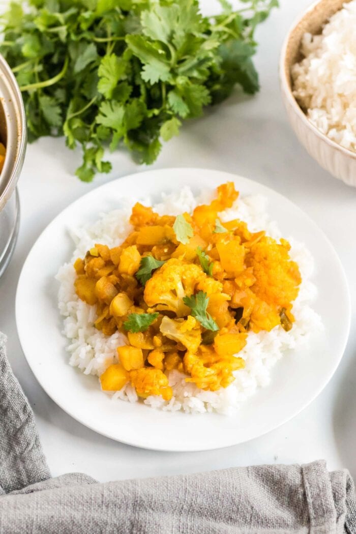 Plate of aloo gobi or curried potato and cauliflower served over a bed of jasmine rice.