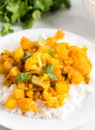 Plate of aloo gobi or curried potato and cauliflower served over a bed of jasmine rice and topped with cilantro.