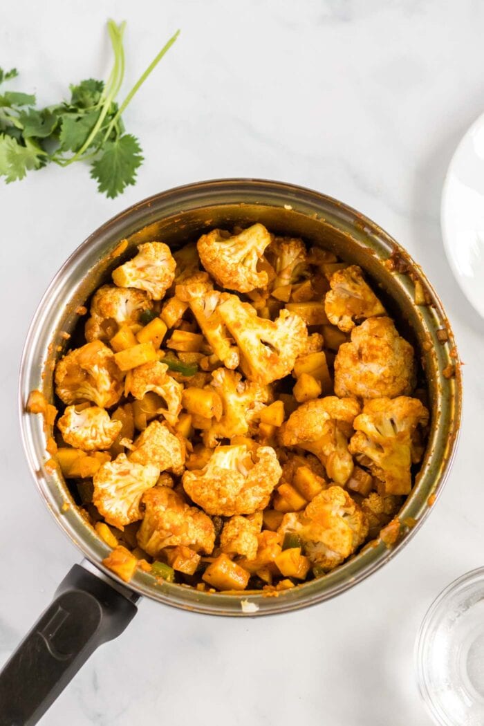 Chopped cauliflower and potato cooking in a curry sauce in a pot.