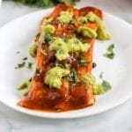 Close up of an enchilada topped with guacamole on a plate.