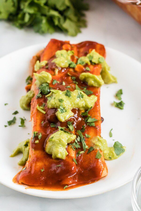 Close up of an enchilada topped with guacamole on a plate.