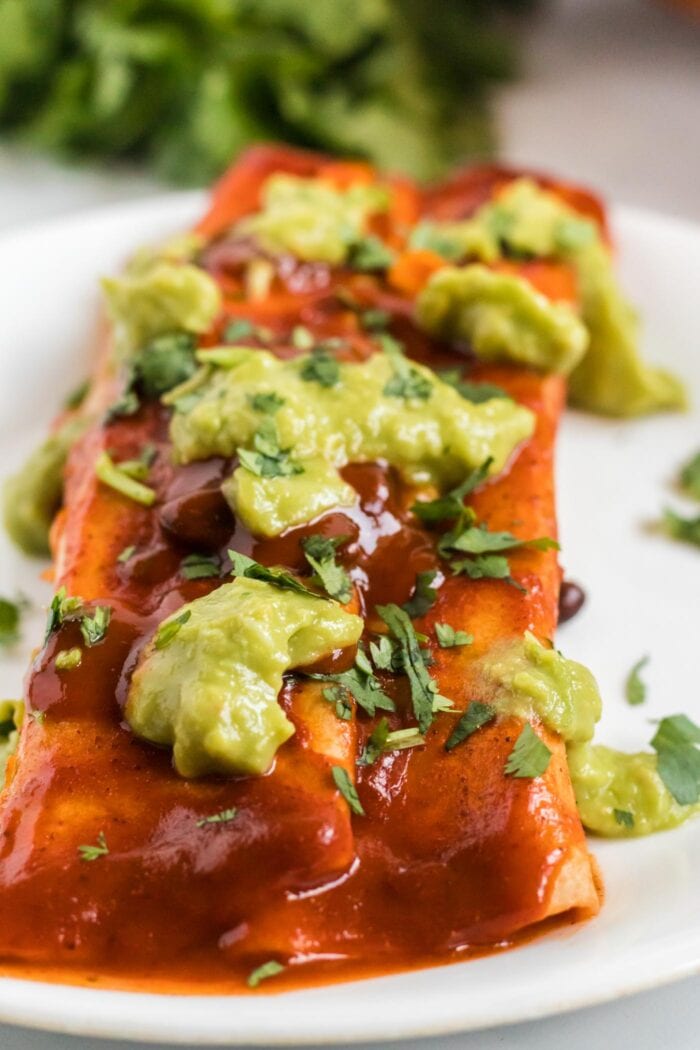 Close up of an enchilada topped with guacamole on a plate.