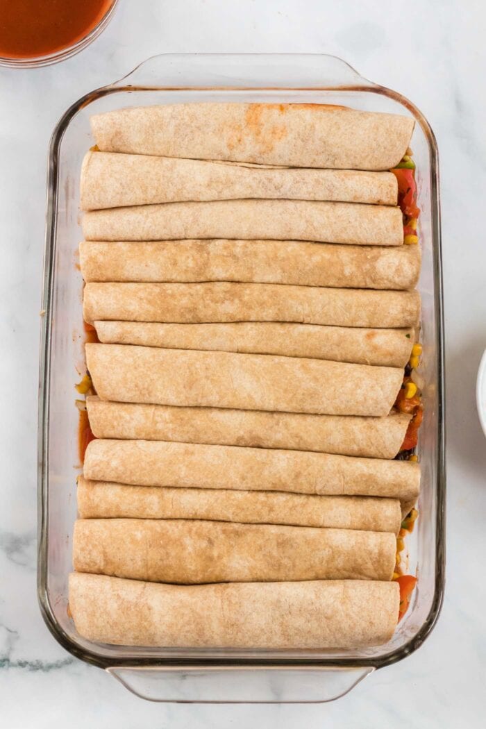 Tortillas rolled up and placed in a baking dish to make enchiladas.