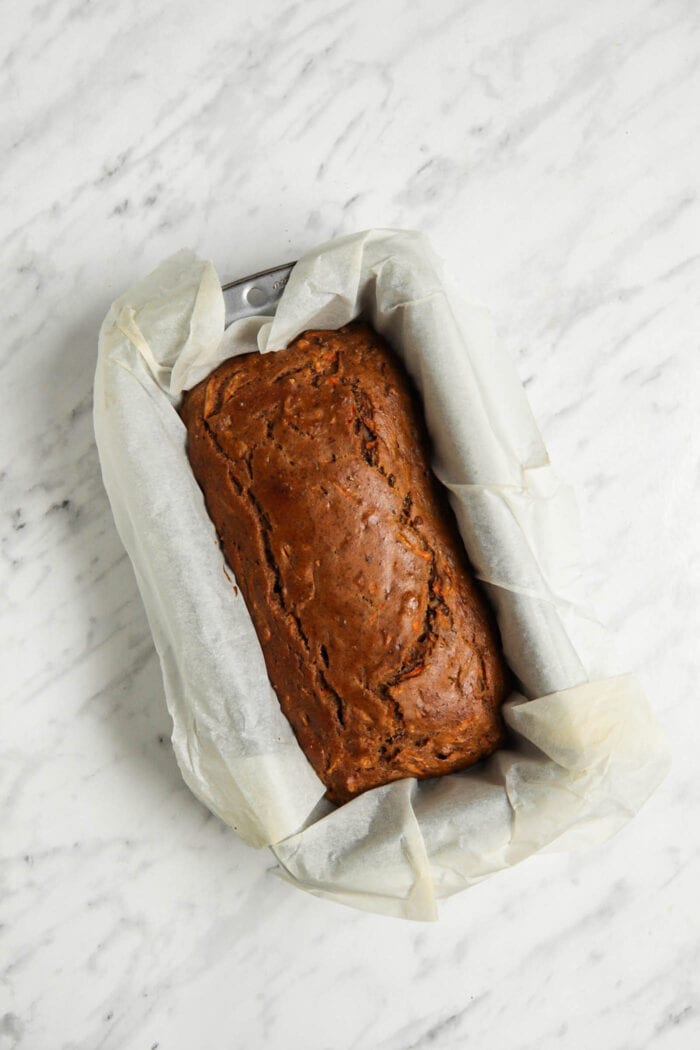 A baked loaf of banana bread in a loaf pan lined with parchment paper.