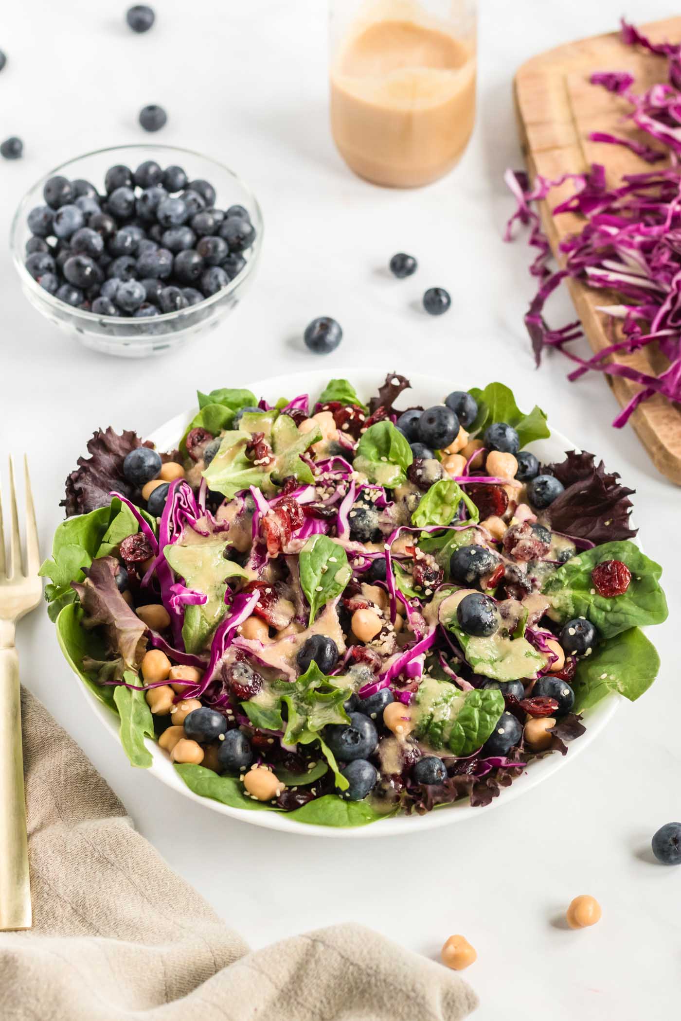 A vibrant, colorful salad composed of mixed greens, shredded red cabbage, and fresh blueberries, with a separate small dish of blueberries nearby.