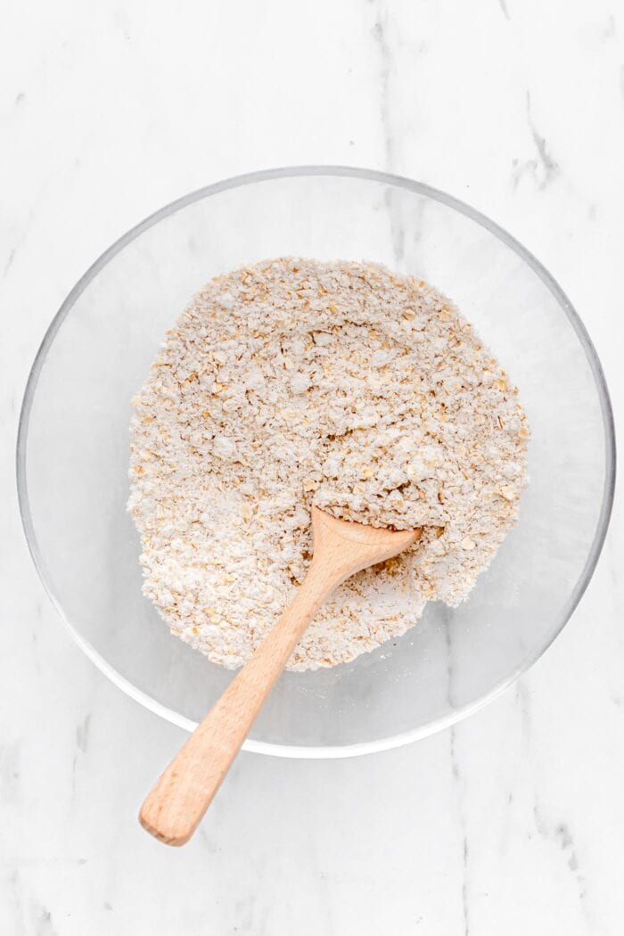 Dry baking ingredients mixed together in a mixing bowl with a wooden spoon.