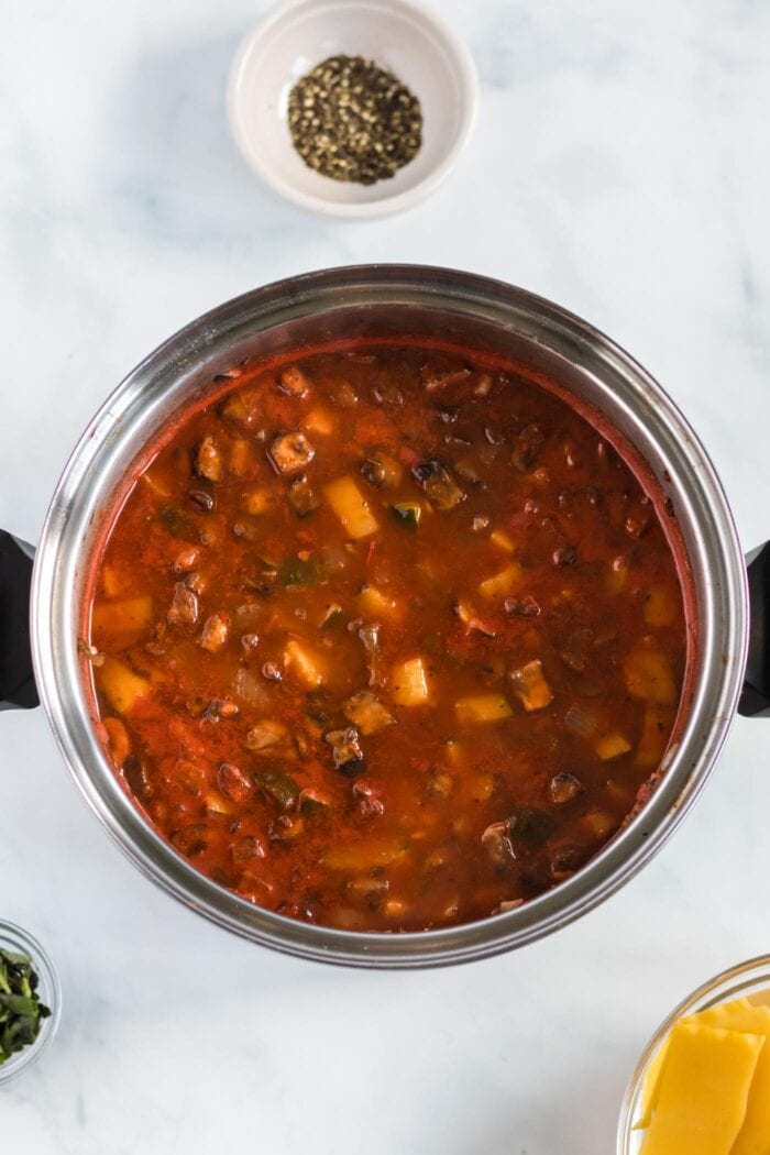 Tomato soup with diced vegetables cooking in a large soup pot.