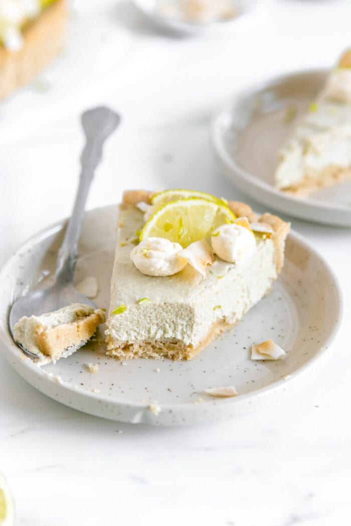 Slice of key lime pie on a plate with a bite taken from it and a fork resting beside it.