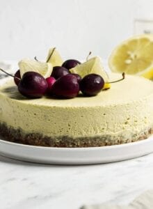 Raw vegan lemon cheesecake topped with cherries and lemon slices on a plate.