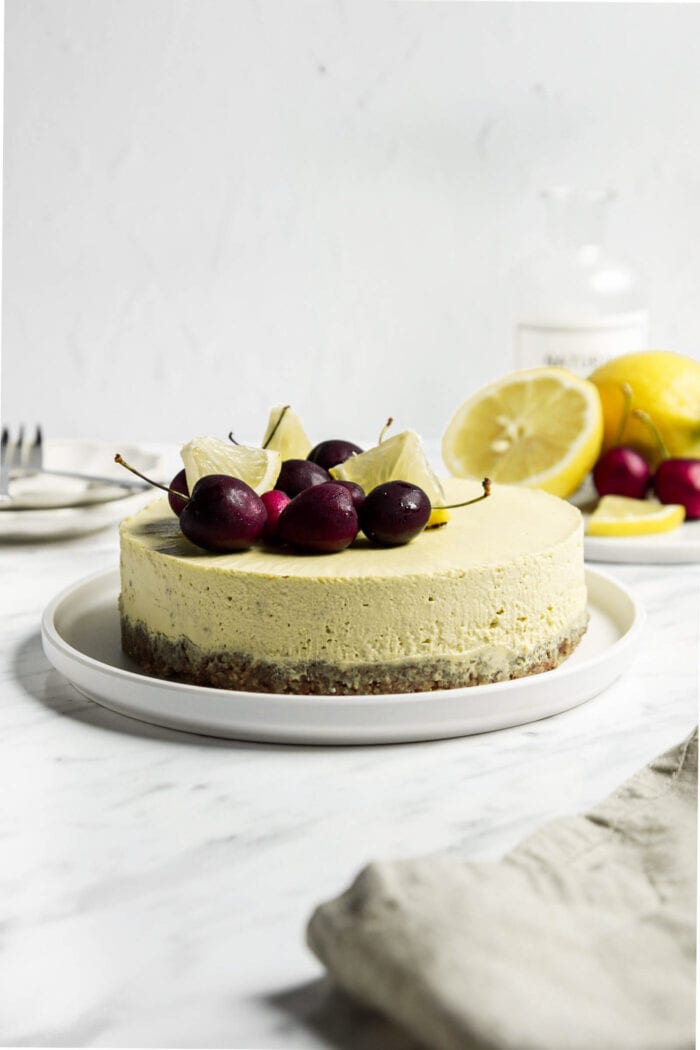 Raw vegan lemon cheesecake topped with cherries and lemon slices on a plate.