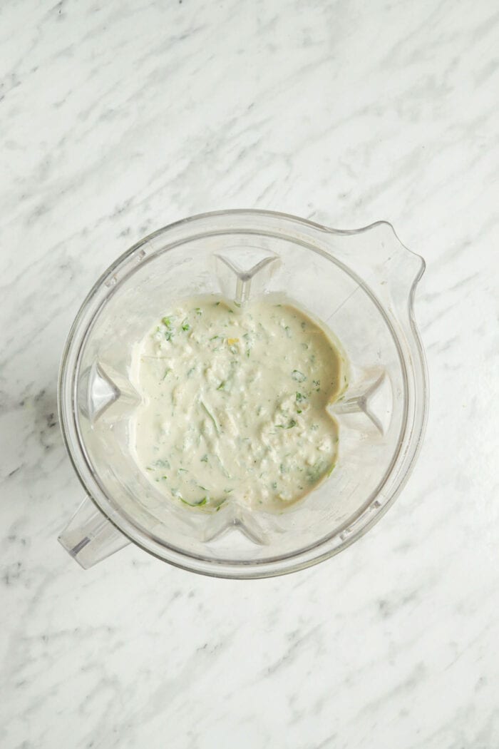 A creamy mixture with spinach in it in a blender container.
