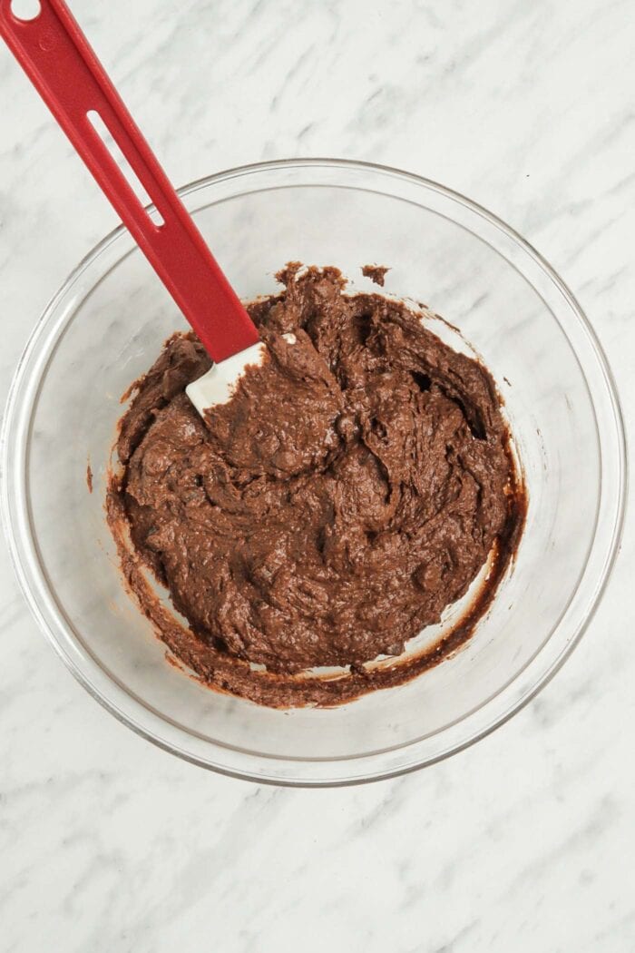 Thick chocolate brownie batter in a glass bowl.