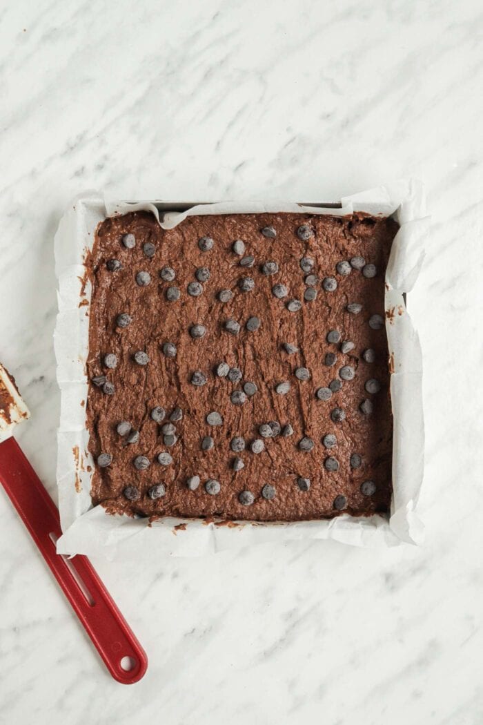 Brownie batter sprinkled with chocolate chips in a baking pan.