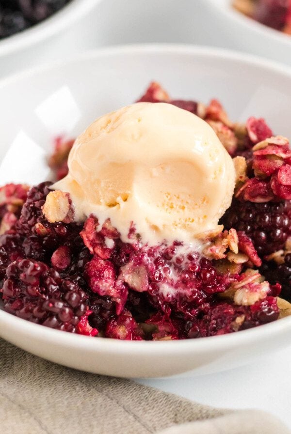 Blackberry crumble topped with a scoop of vanilla ice cream in a bowl.