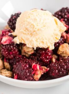 Blackberry crumble topped with a scoop of vanilla ice cream in a bowl.