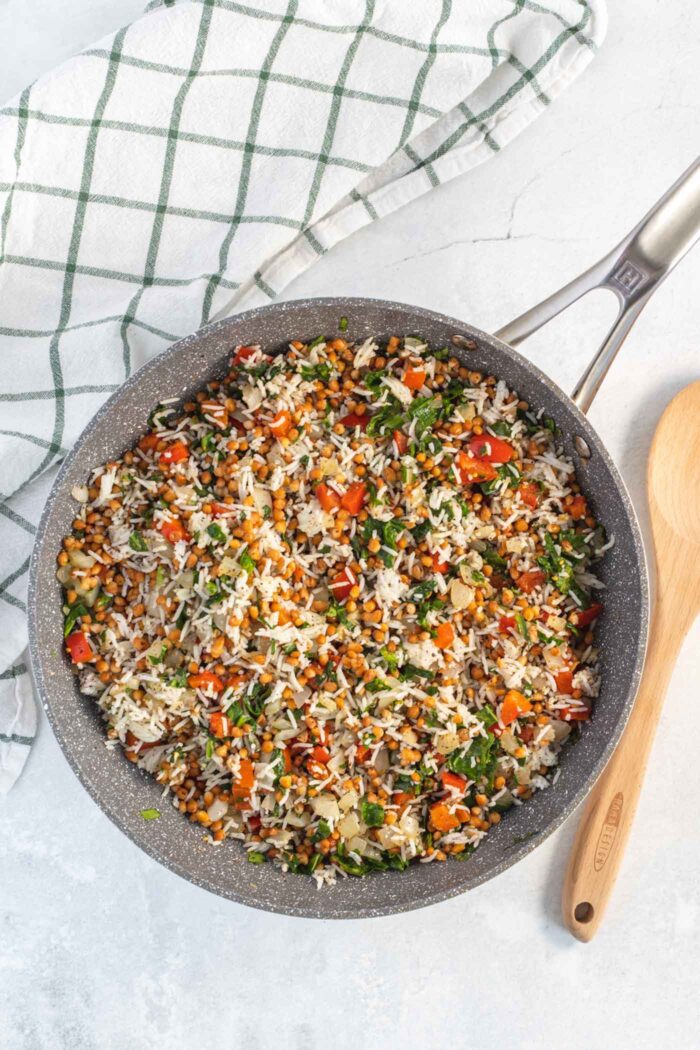 Rice, lentils, spinach and bell peppers cooking in a skillet.