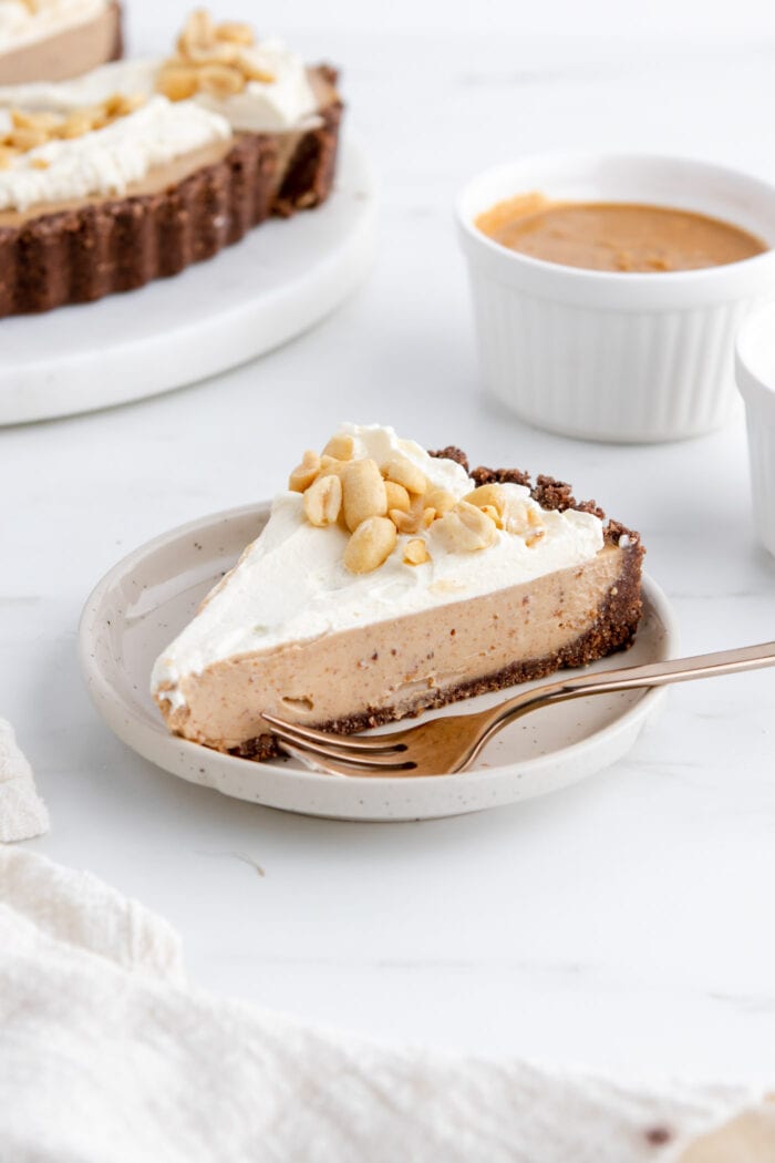 Slice of peanut butter pie topped with whipped cream and peanuts on a plate.