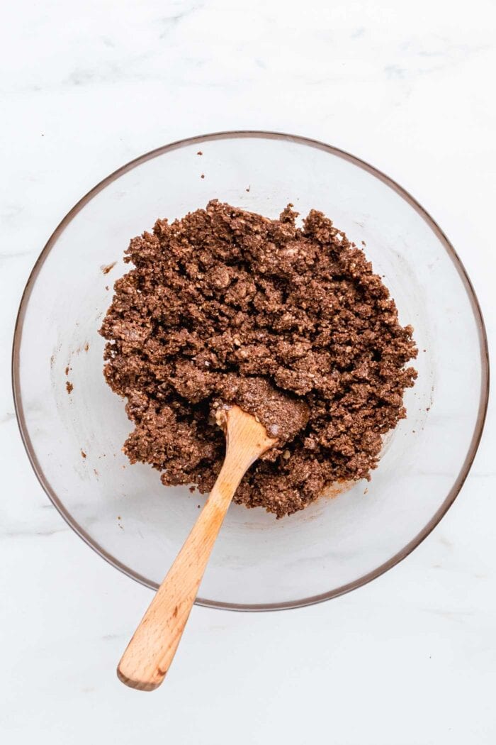 A crumbly chocolate mixture in a bowl with a wooden spoon.