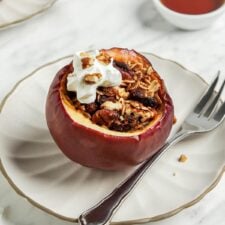 Baked apple stuffed with oats and nuts on a plate topped with a small dollop of whipped cream.