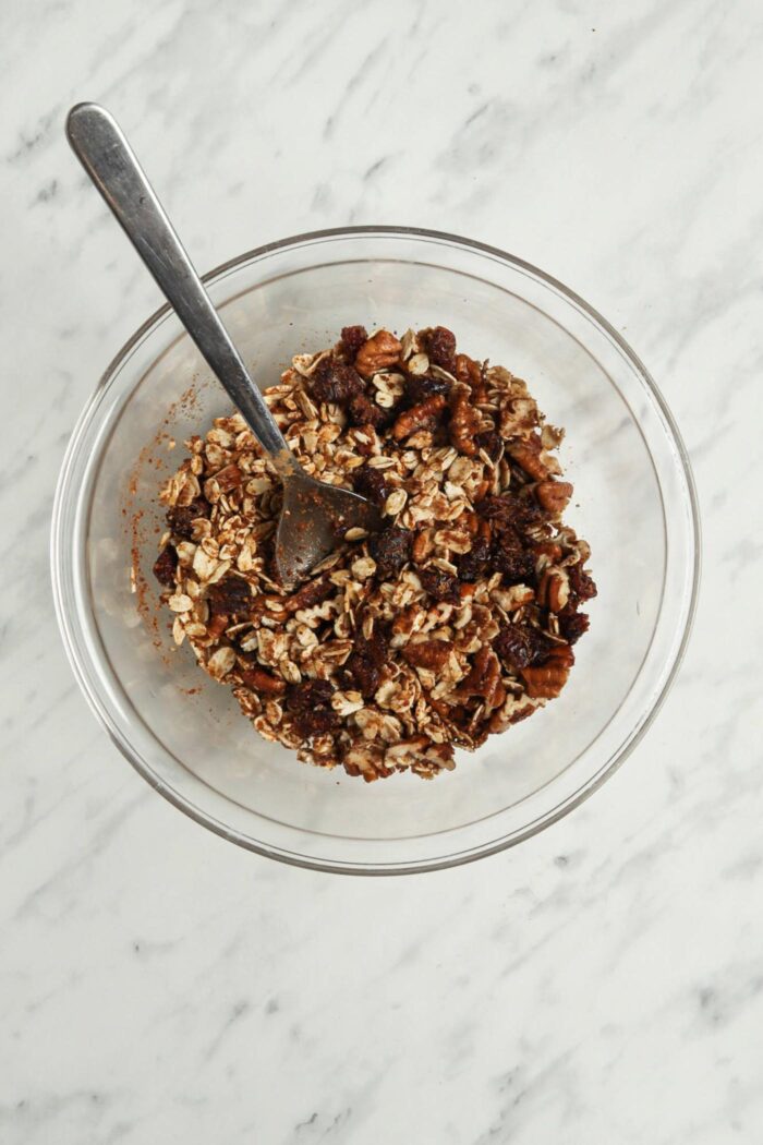 Oats mixed with sugar, nuts and raisins in a bowl.