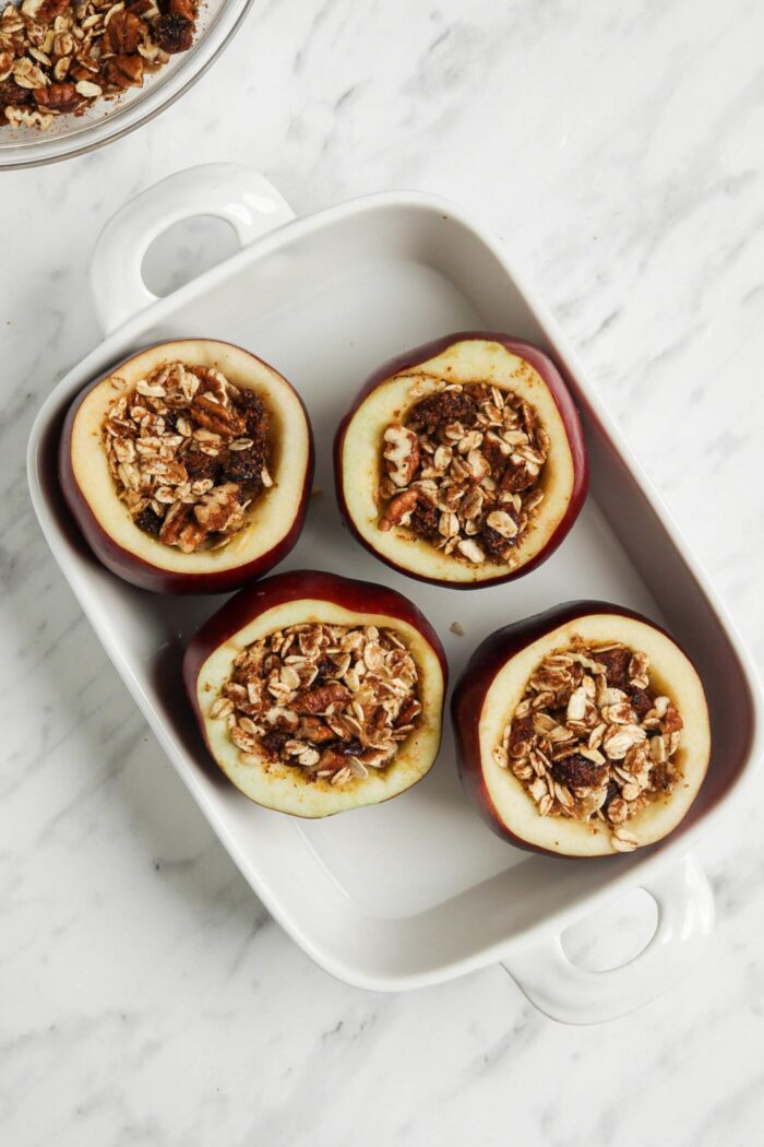 Four stuffed apples in a baking dish.