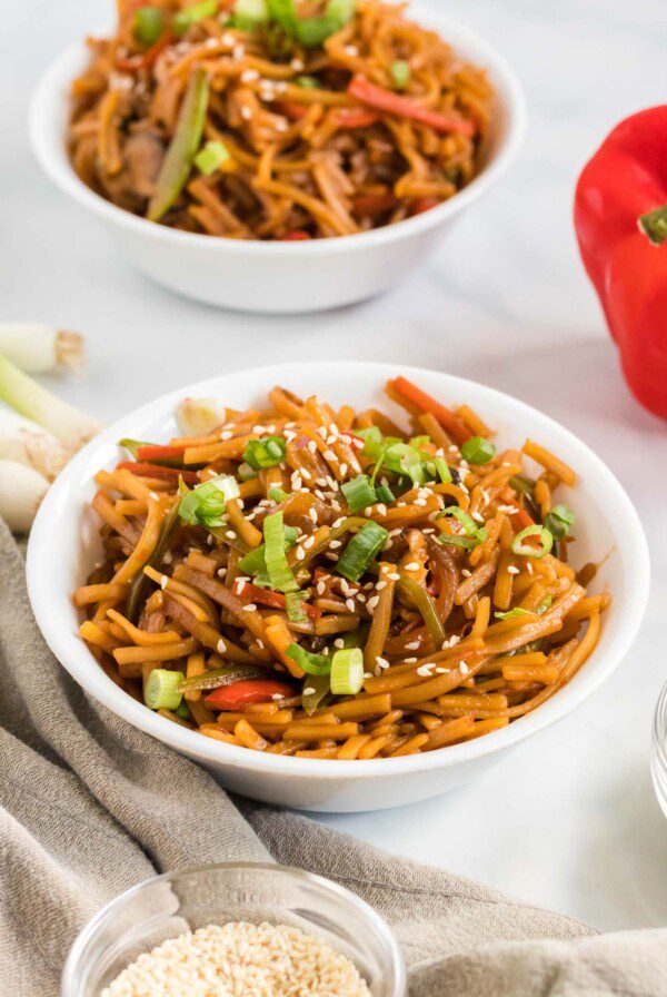 Bowl of vegan low mein noodles topped with green onion and sesame seeds.