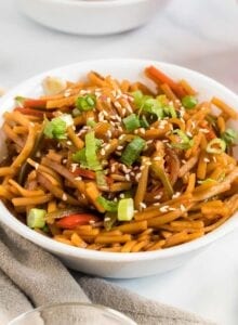 Bowl of vegan low mein noodles topped with green onion and sesame seeds.